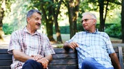 Two men sitting outdoors on a bench, talking.
