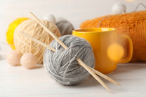 Balls of yarn and a pair of knitting needles with a mug sitting next to them