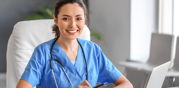 Nurse sitting and smiling with a laptop at a desk.