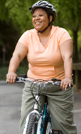 A woman in an orange t-shirt rides a mountain bike in a park.