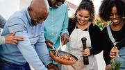 Group of people cooking together, stirring vegetables in a pan with smiles and teamwork.