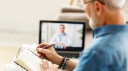 Senior man taking notes during a virtual consultation with a doctor on his laptop at home.