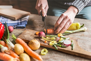 A person chops vegetables with a kitchen knife on a cutting board.