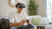 Individual exploring virtual reality entertainment, seated on a sofa with a game controller in hand and headphones nearby.