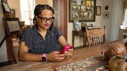 Woman sitting at a table, focused on her smartphone in a cozy, well-lit room.