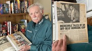 Charles Sasser holding a scrapbook filled with newspaper clippings and photos.