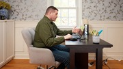 Man sitting at a desk, engaged in a video call on his laptop in a cozy, well-lit room.