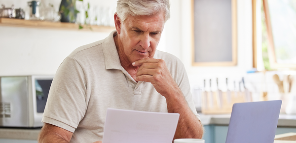 Man looking at statement in kitchen with a laptop.