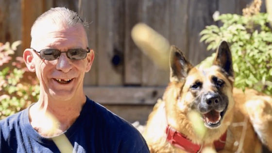 Navy Veteran Benjamin Parsons smiling next to a happy German Shepherd dog with a red collar.