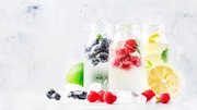 Three glass jars filled with sparkling water and fresh berries, garnished with mint leave.