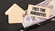 Wooden house cutout next to cash and a tag labeled 'First-Time Homebuyers' on a dark textured surface.