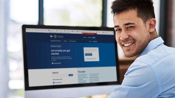 Man with short dark hair looking over his shoulder and smiling, laptop screen showing a blue and white webpage.