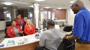 Three healthcare workers in red uniforms assist two elderly men