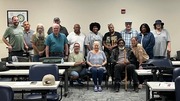 Diverse group of adults posing together in a classroom setting with desks and chairs around them.