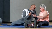 Senior man and woman sitting on gym mats, reviewing a smartphone together after exercise.