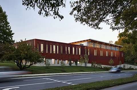 A brown building off the road with green grass and trees. 