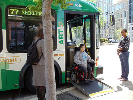 Wheelchair user goes down ramp deployed from Arlington Transit bus on sidewalk.