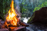  A campfire burning in the woods next to a river. 