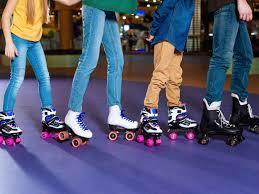 A waist shot of four kids skating in a line on a purple indoor skating rink. 