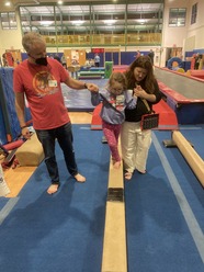 A girl walking across a beam while being supported by a man and woman