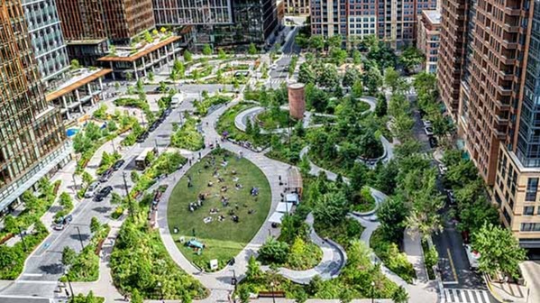 A park featuring trees, a grassy lawn, and trails is surrounded by streets and buildings.