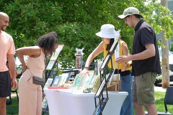 Flourish market; people browsing at outdoor artist table.