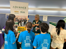 Staff member speaks with students at Edu-Futuro with a NOVA–George Mason partnership banner behind them.