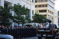 A ceremonial ACPD motorcycle being escorted on the street while police officers stand and salute