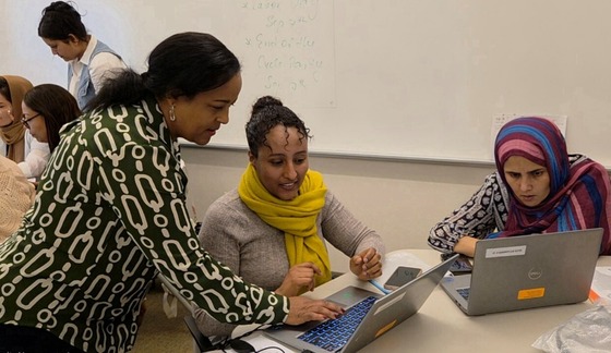 A diverse group of Arlingtonians sits at a table with laptops. An instructor is standing nearby and working with them.