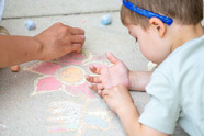 young child drawing a flower with chalk on the sidewalk