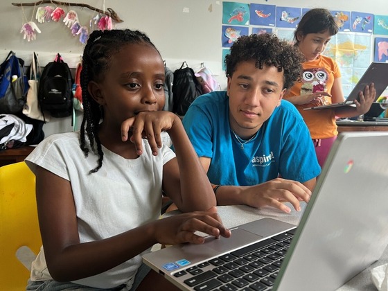 A student uses a laptop while an instructor looks on.