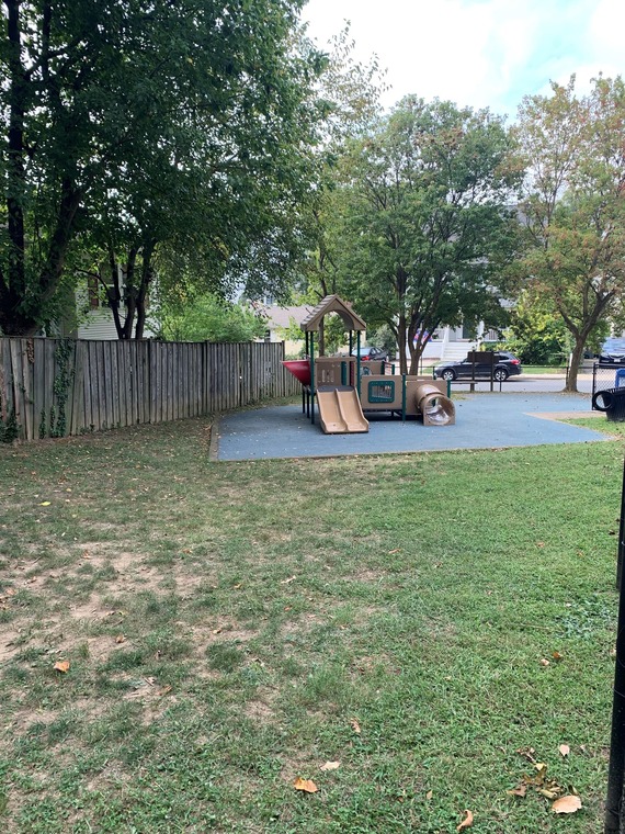 Photo showing a small grassy field with the Slater Park playground in the background.