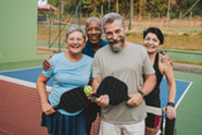 A group of people on a pickleball court holding pickleball paddles.