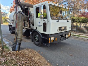 Driver of a leaf collection truck vacuuming leaves from a curb in Arlington.