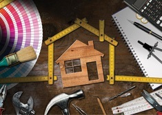Home maintenance tools and a wooden house model on a workbench.