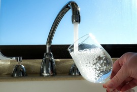Tap water flows out of a faucet into a glass 