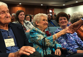 A woman shakes a man's hand at the Centenarian Celebration while another woman looks on