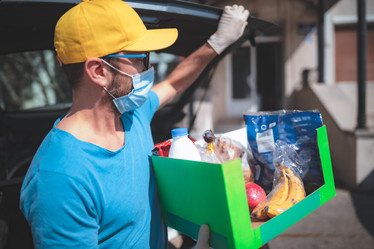 Photograph of man wearing a face mask delivery food assistance box.