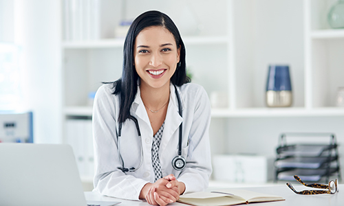 Photograph of female medical provider seated at a desk smiling into the camera. 