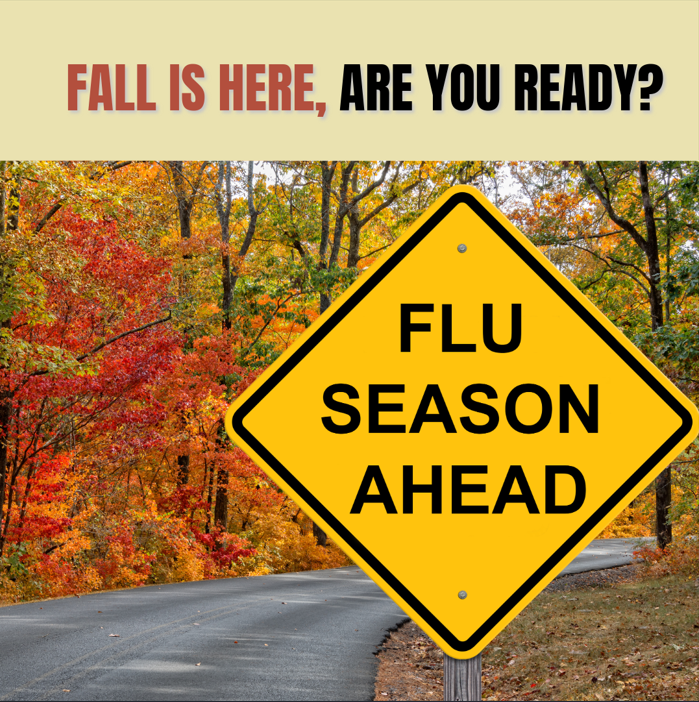 Yellow roadside warning sign reading "Flu Season Ahead" on a road with trees displaying orange and autumn-colored leaves.