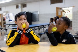 Two students crunch into yummy apples in the school cafeteria. 