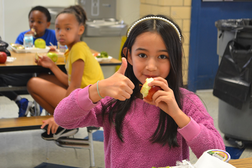 An elementary student takes a bite out of an apple.