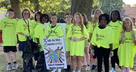 A group of students in matching shirts holding a "Kids in the Community" sign
