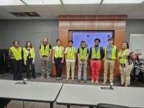 A group of students in reflective yellow vests at a facility tour