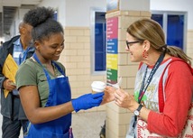 A student handing a teacher a cup of coffee