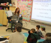 An adult reading a book to a class of elementary students