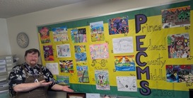 Mr. Satkowski in front of a colorful display of student artwork.