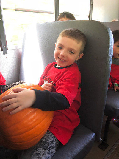 photograph of boy holding pumpkin on school bus