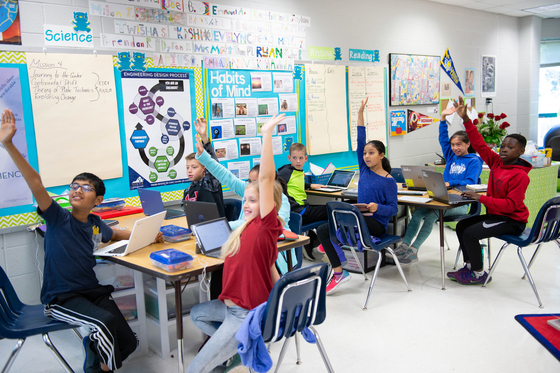 Students in classroom raising hands
