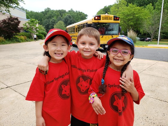 three kindergarten students posing before boarding the field trip bus